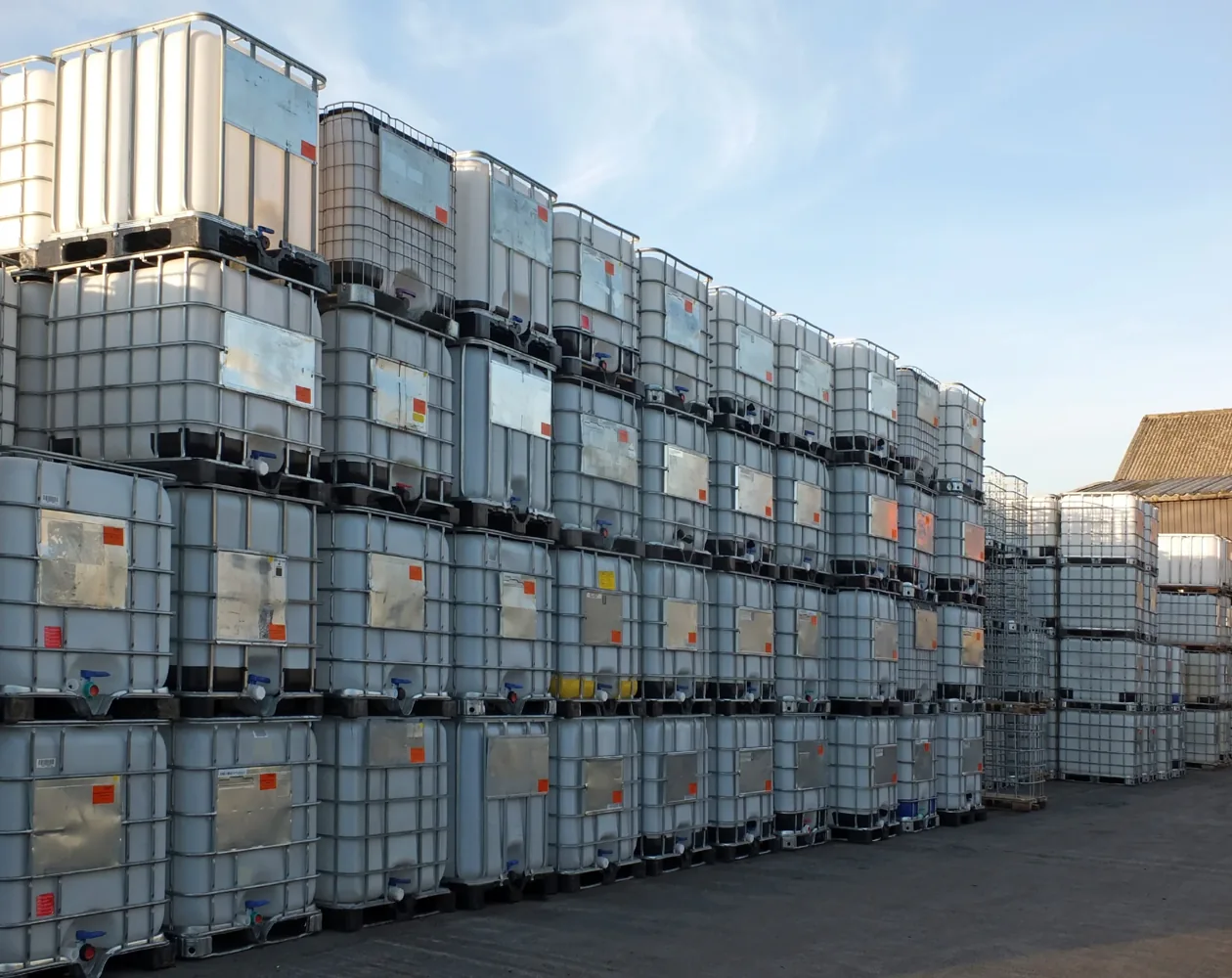 Used intermediate bulk containers stacked in an outdoor handling area.