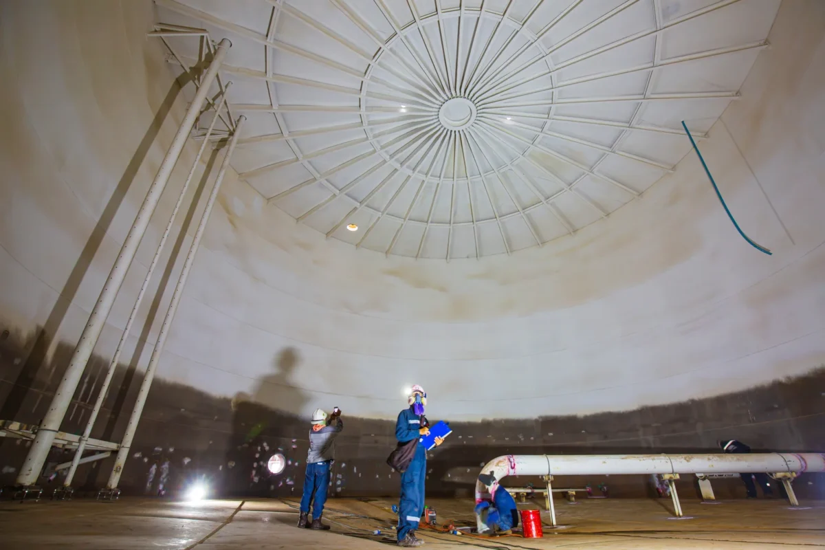 Workers inspecting the interior of a large steel fuel storage tank.