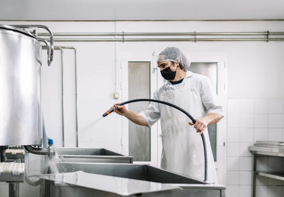 Worker washing stainless steel dairy equipment with a hose